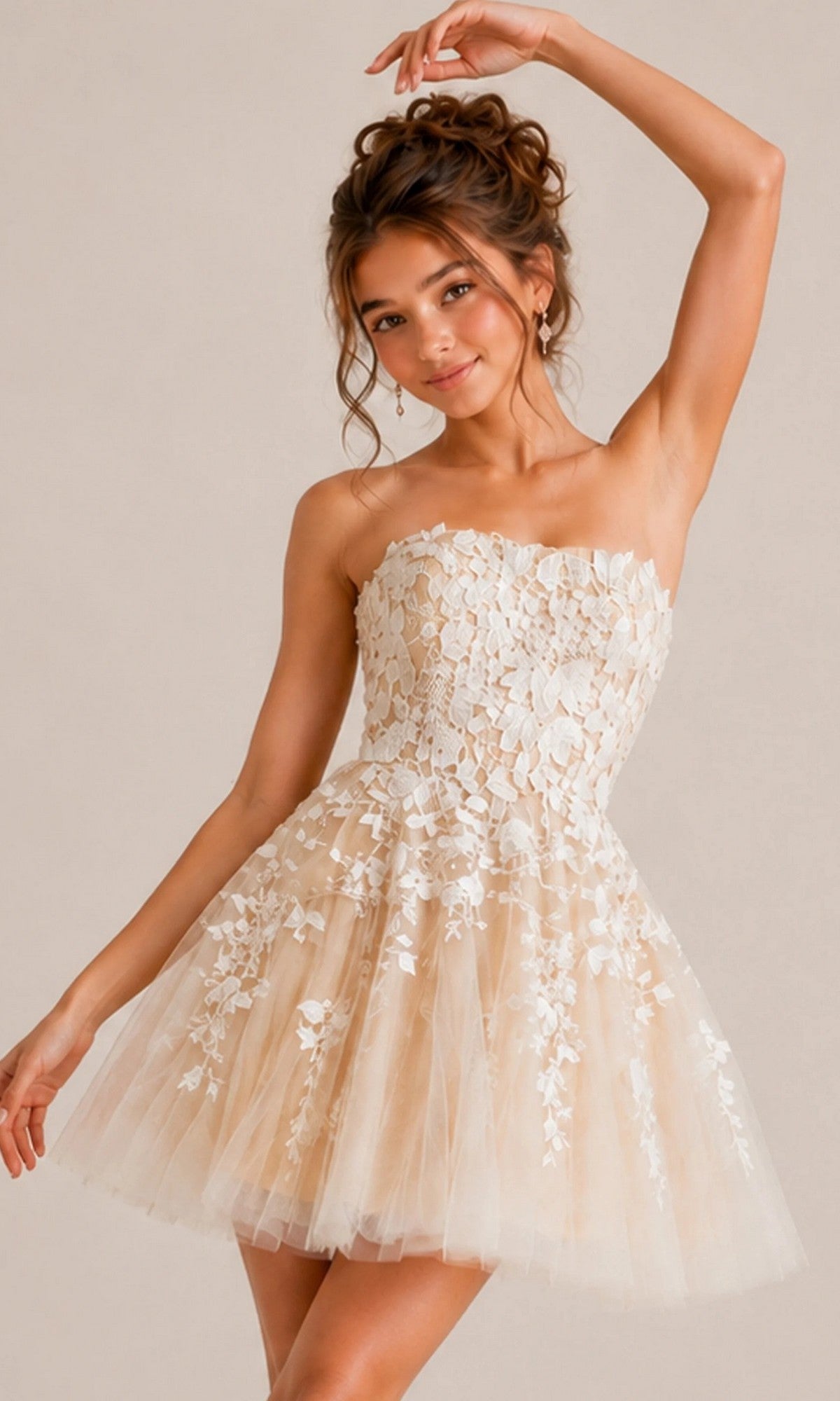 A woman poses with one arm raised and her hair in a loose bun, wearing the Jovani 1830 Short Homecoming Dress—a strapless, beige tulle dress adorned with white floral lace appliques.