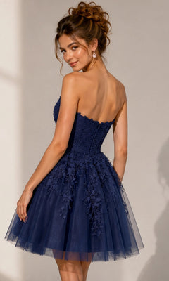 A woman wearing the Short Homecoming Dress: Jovani 1830—a navy blue, strapless, knee-length fit-and-flare dress adorned with delicate floral lace appliques and intricate floral embroidery—stands and glances over her shoulder.