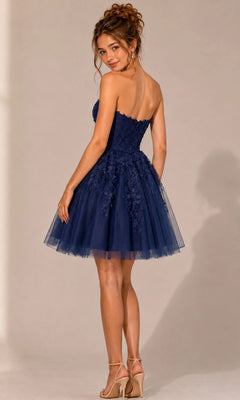 A woman stands on a plain background, facing slightly away, wearing the Jovani 1830 Short Homecoming Dress in navy blue—a strapless fit-and-flare style crafted from lace and tulle with detailed floral lace appliqués.