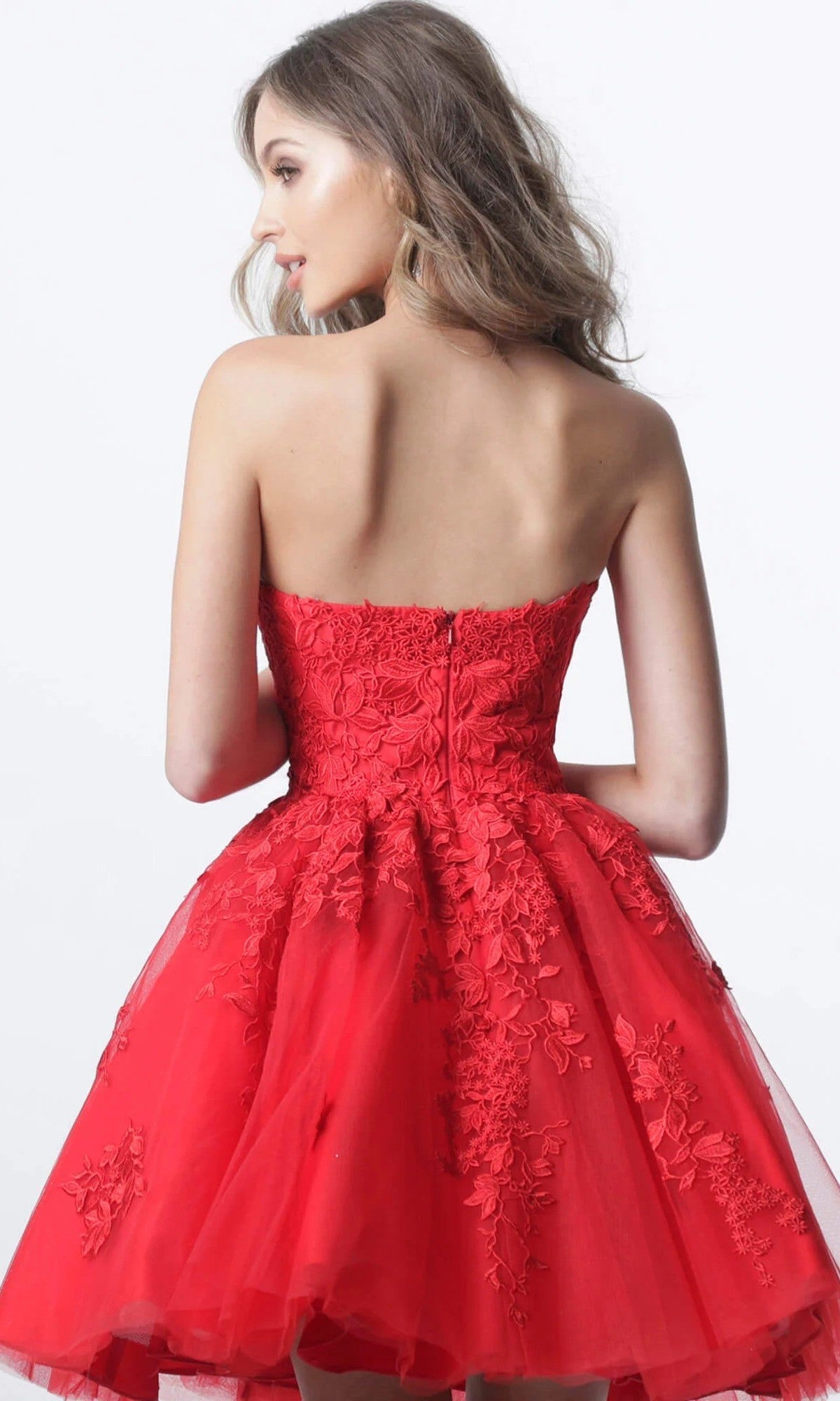 A woman is seen from the back against a plain white background, wearing Jovani 1830—a strapless, short, bright red fit-and-flare homecoming dress featuring exquisite floral lace appliques and floral embroidery.