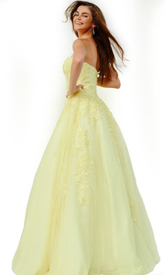 A woman wearing the Jovani 1831 Long Formal Dress—a strapless, pale yellow ballgown with lace details—smiles and turns slightly to her left against a white background.