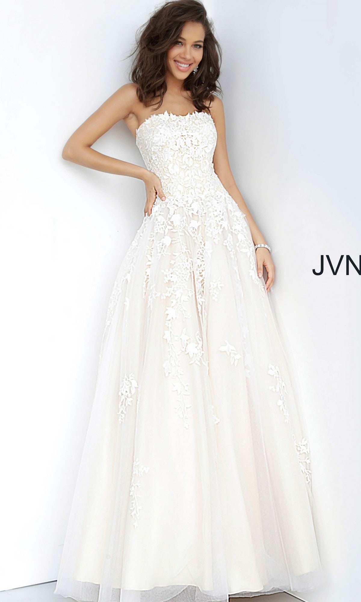 A woman stands and smiles against a plain light background, wearing the Long Formal Dress: Jovani 1831 in off white/nude—a strapless, floor-length ballgown featuring elegant floral lace details.