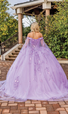 A person with blonde hair stands outdoors, facing away from the camera, wearing the Quinceanera Dress 1840 By Dancing Queen—a long, lavender off-the-shoulder ball gown with floral details.