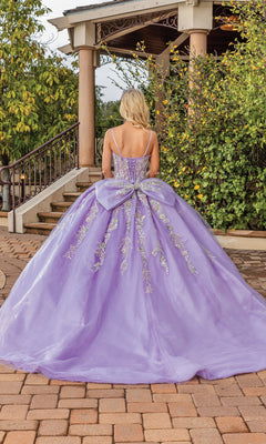 A woman stands outdoors in the Quinceanera Dress 1848 By Dancing Queen, an a-line lavender ball gown with floral embroidery and a large bow back, her elegant silhouette captured from behind.