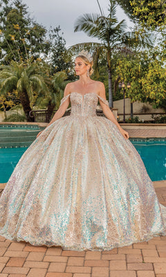 A woman stands by a pool, wearing the Quinceanera Dress 1854 by Dancing Queen, featuring an off-the-shoulder design and a full, sparkling skirt. Palm trees and lush greenery form a stunning backdrop.