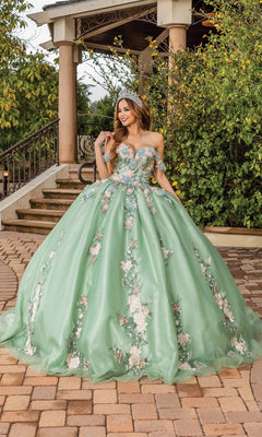 A woman stands outdoors in the Quinceanera Dress 1856 By Dancing Queen, a sage green gown with floral embellishments and a tiara, posing in front of steps and greenery.
