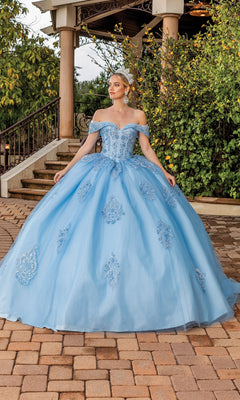 A woman stands outdoors wearing the Quinceanera Dress 1863 By Dancing Queen, a light blue ball gown with off-the-shoulder sleeves, lace applique details, a full skirt, paired with a tiara and earrings.