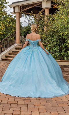 A woman wearing the Quinceanera Dress 1867 By Dancing Queen in aqua blue stands outdoors, facing away near stairs and greenery; the off-the-shoulder ball gown features a full skirt.