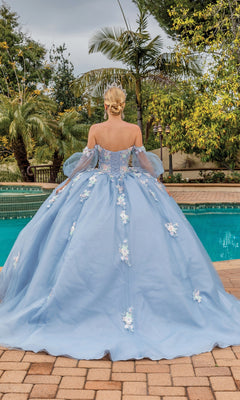 A person with blonde hair in an updo wears the Quinceanera Dress 1871 By Dancing Queen, a light blue a-line ball gown with lace floral applique, standing by a swimming pool with trees in the background.