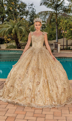 A woman poses by a pool in the Quinceanera Dress 1877 By Dancing Queen, featuring a gold full skirt, sequin details, removable puff sleeves, and a matching tiara. Palm trees and lush greenery create an elegant backdrop.
