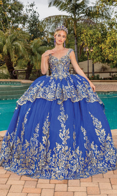 A woman in the Quinceanera Dress 1881 By Dancing Queen, featuring royal blue fabric and gold lace applique, stands on a patio near a pool, wearing a tiara and surrounded by greenery.