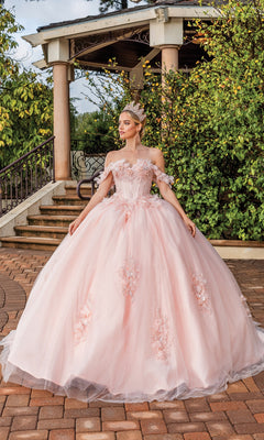 A woman in the Quinceanera Dress 1883 By Dancing Queen, a pink off-the-shoulder A-line ball gown, with a crown, stands on a brick pathway before a gazebo surrounded by greenery.