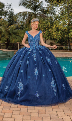 A woman in the Quinceanera Dress 1886 By Dancing Queen, adorned with floral embroidery and a tiara, stands on a patio near a pool surrounded by greenery.