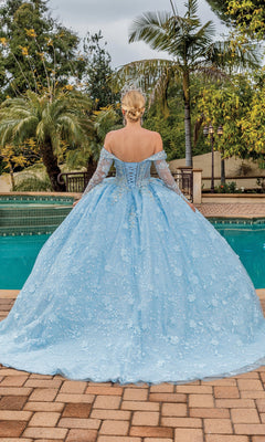 A woman with blonde hair stands by a pool in the Dancing Queen Quinceanera Dress 1890, an elegant light blue off-the-shoulder ball gown. Palm trees sway gently in the background as she faces away from the camera.