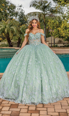 A woman stands by a pool in front of palm trees, wearing the Quinceanera Dress 1897 By Dancing Queen—a pastel off-shoulder gown with silver embroidery and a sparkling silver tiara.