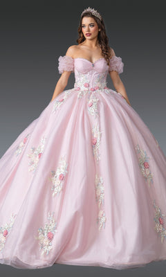 A woman wearing the Quinceanera Dress 1900 By Dancing Queen in blush, featuring a tulle ballgown skirt with 3D floral appliques and off-shoulder puff sleeves, paired with a tiara and standing against a plain grey background.