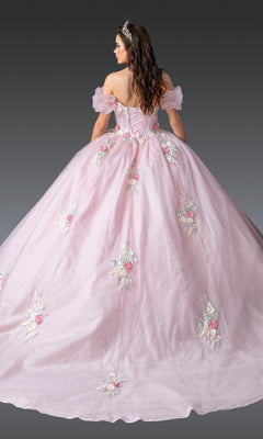 Wearing the Quinceanera Dress 1900 By Dancing Queen, a woman stands facing away and showcases the gown’s voluminous pastel pink tulle ballgown skirt and elegant corset-style back adorned with intricate 3D floral appliques.