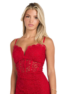 A woman with long blonde hair wears the Long Red Lace Prom Dress: Morgan 19069, featuring thin straps and a sheer lace bodice, standing against a white background.