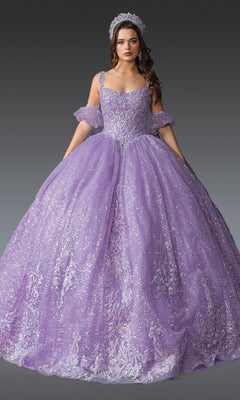 A woman is wearing the Quinceanera Dress 1907 by Dancing Queen in lilac, a glittering ballgown adorned with floral details and a matching tiara, featuring detachable off-shoulder sleeves, as she stands against a plain gray background.