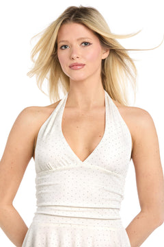 A woman with long blonde hair wears the Morgan 19282 short homecoming dress—a sleeveless, white deep v-neck halter dress with small black dots—while standing against a white background.