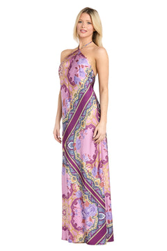 A woman wearing the Paisley Floral Printed Maxi Dress: Morgan 19309, featuring a sleeveless halter neckline and a vibrant pink, purple, and yellow patterned design, stands facing slightly to the side.