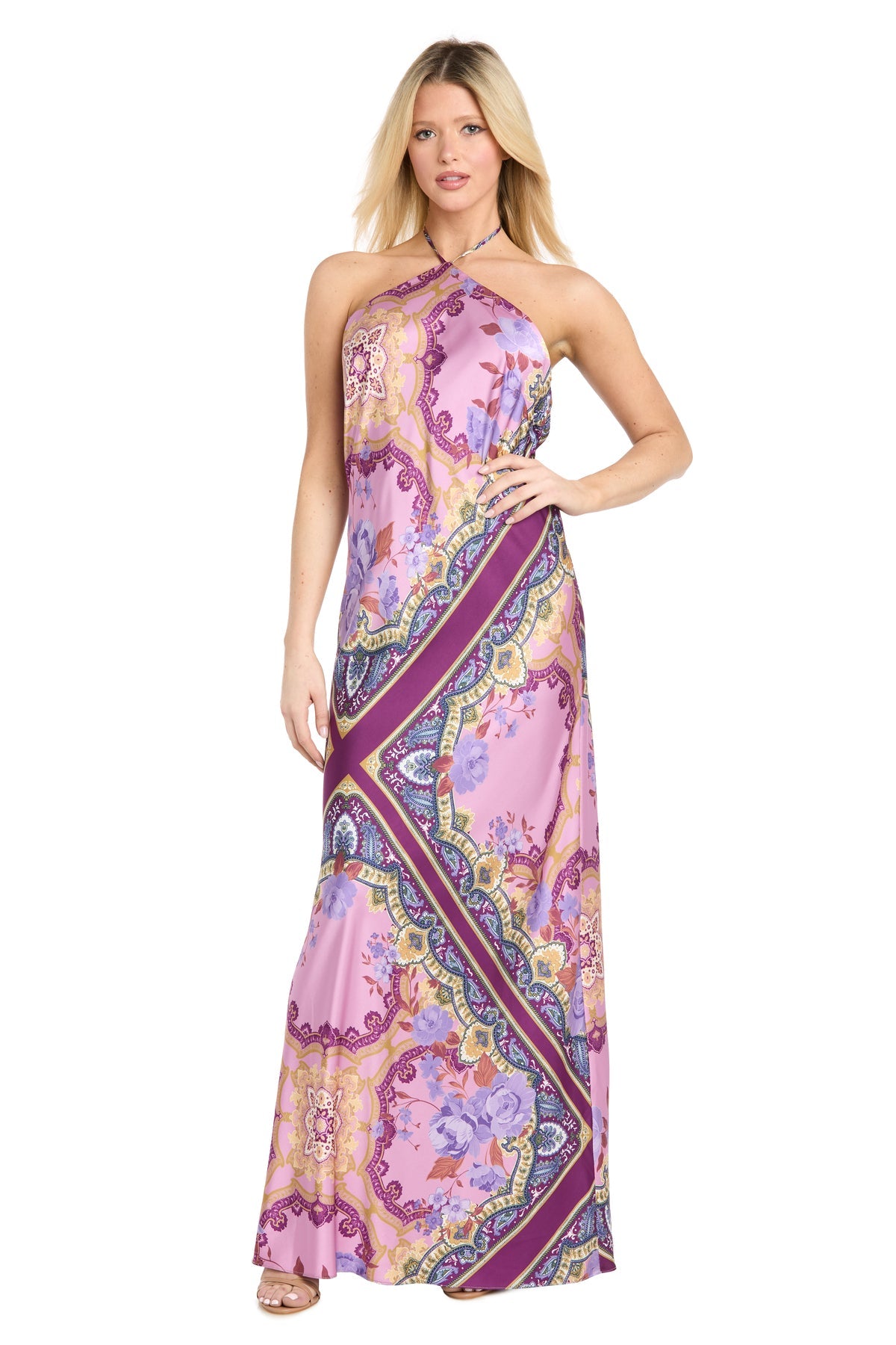 A woman wearing the Paisley Floral Printed Maxi Dress: Morgan 19309, a long sleeveless maxi dress featuring a pink, purple, and yellow paisley pattern and a halter neckline, stands facing forward.
