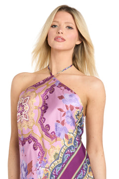 A woman wearing the Paisley Floral Printed Maxi Dress: Morgan 19309, featuring a halter neckline and purple patterned fabric with floral and geometric designs, stands against a white background.