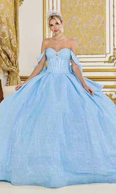 A woman poses in an ornate gold and white room wearing the Quinceanera Dress 1937 By Dancing Queen, a sparkling light blue glitter ball gown with off-the-shoulder straps and a tiara.