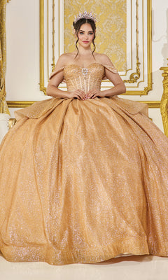 A woman in the Quinceanera Dress 1937 By Dancing Queen, featuring glitter and off-the-shoulder straps, wears a tiara while standing in an ornately decorated gold and white room.