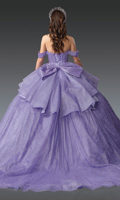 A woman with long brown hair models the Quinceanera Dress 1937 By Dancing Queen, a sparkling lavender ball gown with layered tulle, off-the-shoulder straps, and a large back bow, set against a gray background.