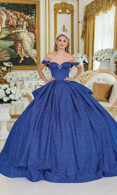 A woman in the Quinceanera Dress 1937 by Dancing Queen, featuring off-the-shoulder straps and a glittering ball gown, stands in an ornate room with gold accents and white floral arrangements, wearing a crown.