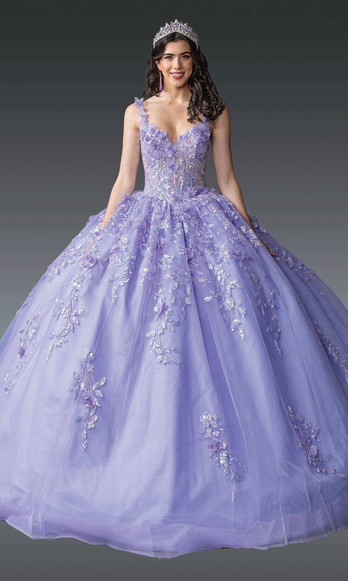 A woman in the Quinceanera Dress 1948 By Dancing Queen, featuring a lavender 3D flower design with a corset bodice and ball gown skirt, smiles against a gray background while wearing a tiara.