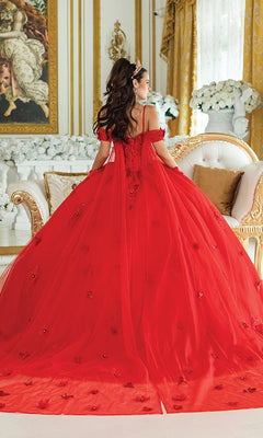 A woman wearing the Quinceanera Dress 1954 By Dancing Queen—a glitter tulle ball gown with a lace corset bodice—stands with her back to the camera in an ornate, gold-accented room with white floral arrangements.