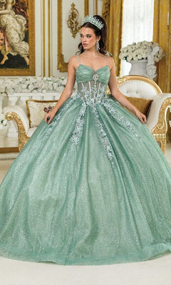 A woman in the Long Quinceañera Dress with Bow: Dancing Queen 1958, a sparkling mint green gown with floral details and a tiara, stands in an ornately decorated room adorned with gold accents and white flowers.
