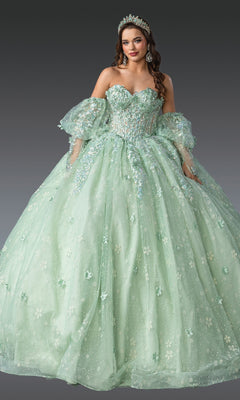 A woman wears the Quinceanera Dress 1966 by Dancing Queen—a sparkling light green gown with puffed sleeves, intricate beading, and a tiara—standing against a plain gray background.