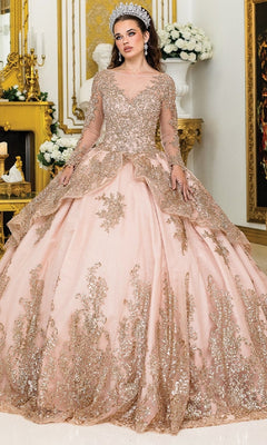 A woman in the Quinceanera Dress 1968 by Dancing Queen, featuring pink fabric, gold lace details, and sparkly embellishments, stands in an ornate room with gold decor and white floral arrangements, wearing a jeweled crown.