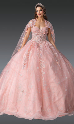 A woman stands against a dark background wearing the Quinceanera Dress 1970 By Dancing Queen—an embellished light pink ball gown with 3D flowers, floral details, a matching cape, and a tiara.
