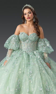 A woman in the Quinceanera Dress 1973 by Dancing Queen—a light green, off-the-shoulder gown with floral embroidery, sheer puff sleeves, corset bodice, and matching gloves—completes her look with a tiara and earrings.