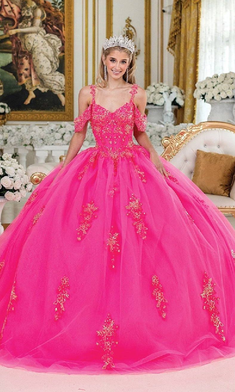 A woman wearing the Hot Pink Quinceanera Dress 1983 By Dancing Queen, featuring gold embellishments and a corset bodice, smiles in an ornate, flower-filled room with a sparkling tiara.