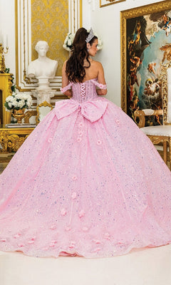 A woman wears the Quinceanera Dress 1984 by Dancing Queen, featuring sparkly pink fabric and a large bow, as she stands in an ornate room filled with classical decor and artwork, facing away from the camera.