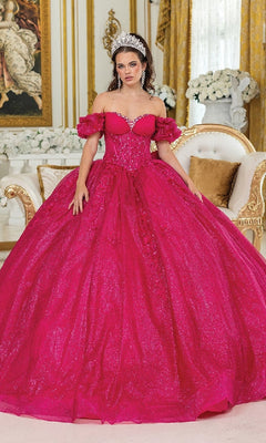A woman wears the Quinceanera Dress 1985 By Dancing Queen, a sparkling bright pink ball gown with a corset bodice and tiara, standing in an ornate gold room with a white sofa and floral arrangements.