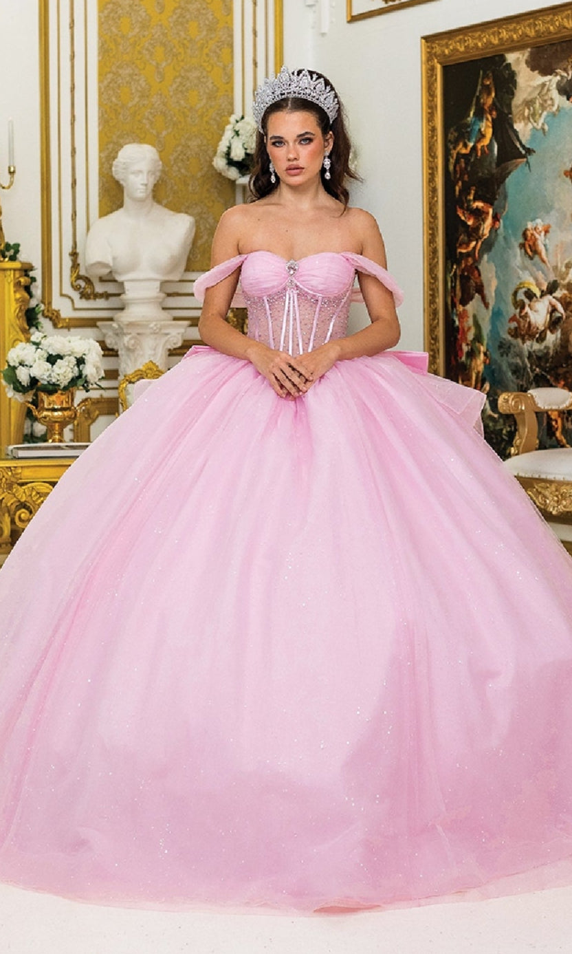 A woman wears the Quinceanera Dress 1996 By Dancing Queen—a glitter tulle ball gown with off-the-shoulder sleeves and a tiara—standing in an ornate room with gold decor and classical artwork.