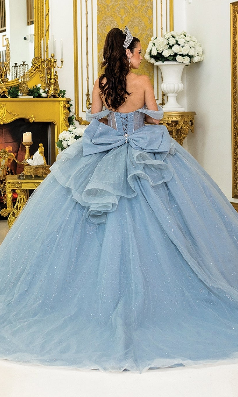 A woman faces away from the camera in an ornate, gold-decorated room, wearing the Quinceanera Dress 1996 By Dancing Queen—a glitter tulle ball gown with a large bow—standing before an elaborate fireplace.
