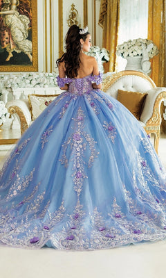 A woman in the Blue Quinceanera Dress 1999 By Dancing Queen, featuring a tiara and purple floral embellishments, stands in an elegant gold-decorated room.