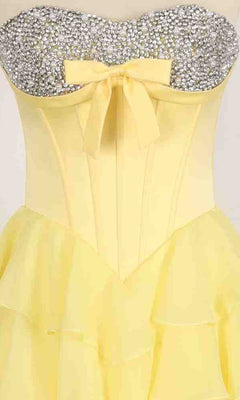 The PromGirl Exclusive 250203 is a strapless yellow ball gown with a layered skirt, fitted corset bodice adorned with silver rhinestones, and a charming yellow bow at the waist.