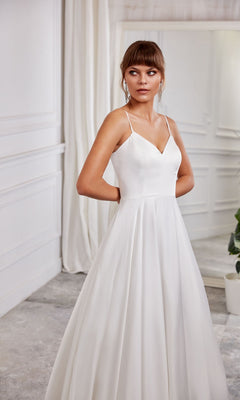 A woman in the Long White Dress: Aerie Couture 2000, featuring an a-line skirt, stands indoors in a light-colored room, looking to her side.