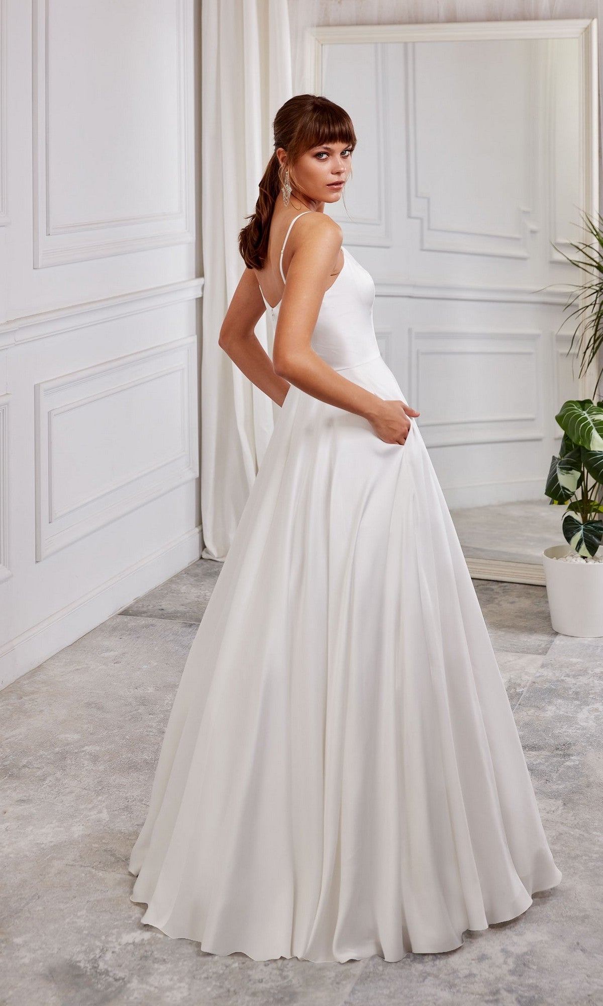 A woman wearing the Long White Dress: Aerie Couture 2000 with an a-line skirt stands in a paneled white room, glancing over her shoulder at the camera.