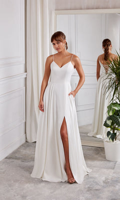 A woman wearing the Aerie Couture 2001 Long White Dress in Diamond White, featuring an a-line skirt and thin straps, stands indoors near a mirror and a potted plant.
