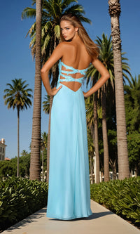 Woman in a light blue dress with cut-out back standing in front of palm trees.