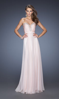 A woman wears the La Femme Designer Pleated Chiffon Prom Dress 20027, a floor-length, strapless pale pink gown featuring a sweetheart neckline and jeweled embellishments.